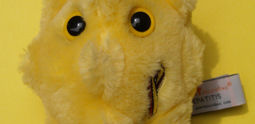 A photo of a stuffed toy representing hepatitis. It is a bright yellow ball with ridges, and has two big yellow eyes.