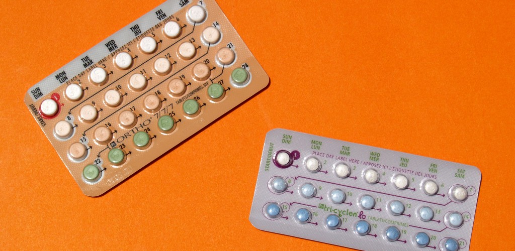 A photo of 2 packs of the birth control pill. One is a 28 pill package, and one is a 21 pill package. They are on an orange background.